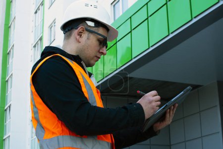 Foto de Constructor inspecciona el nuevo edificio, anotando los comentarios en la tableta.. Planta de construcción comprobar el dibujo y el flujo de trabajo empresarial de la nueva casa de gran altura. - Imagen libre de derechos