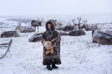 The Yamal Peninsula. Reindeer with a young reindeer herder. Happy boy on reindeer herder pasture playing with a toys in winter.