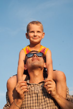 Foto de El hijo de su padre bajo un cielo hermoso, un niño juega con papá, el niño se prueba las gafas de sol - Imagen libre de derechos