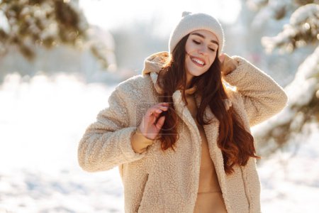 Mujer con estilo disfrutando de los momentos de invierno en un parque nevado. Mujer joven en ropa de invierno posando con alegría afuera, día helado. Juventud, moda, estilo de vida y concepto de ocio.