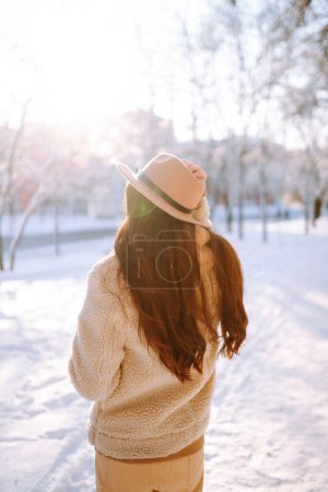 Mujer con estilo disfrutando de los momentos de invierno en un parque nevado. Mujer joven en ropa de invierno posando con alegría afuera, día helado. Juventud, moda, estilo de vida y concepto de ocio.