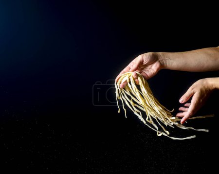 Hand throwing egg noodles on dark background, Flying cooked pasta in hands over black. Creative advertisement, advert concept for Italian macaroni pasta noodles. Copy space banner.