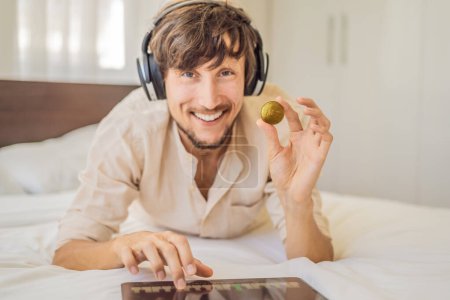 Young man, a digital artist, DJ creates digital art on a tablet at home and shows a coin with the inscription NTF - non fungible token. Remote work, digital nomad, digital painting, animation, video