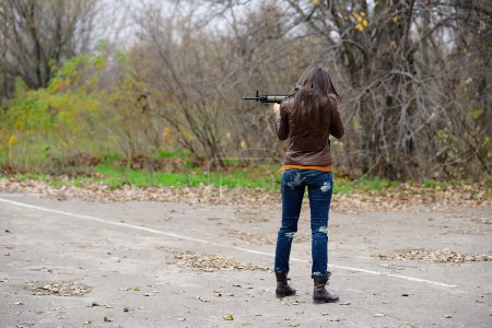 Téléchargez les photos : Une fille avec une arme automatique, regarde à travers la portée, la vue de l'arrière - en image libre de droit